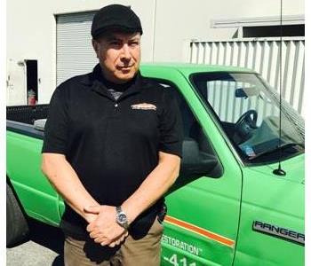 male employee with black shirt and hat in front of green truck